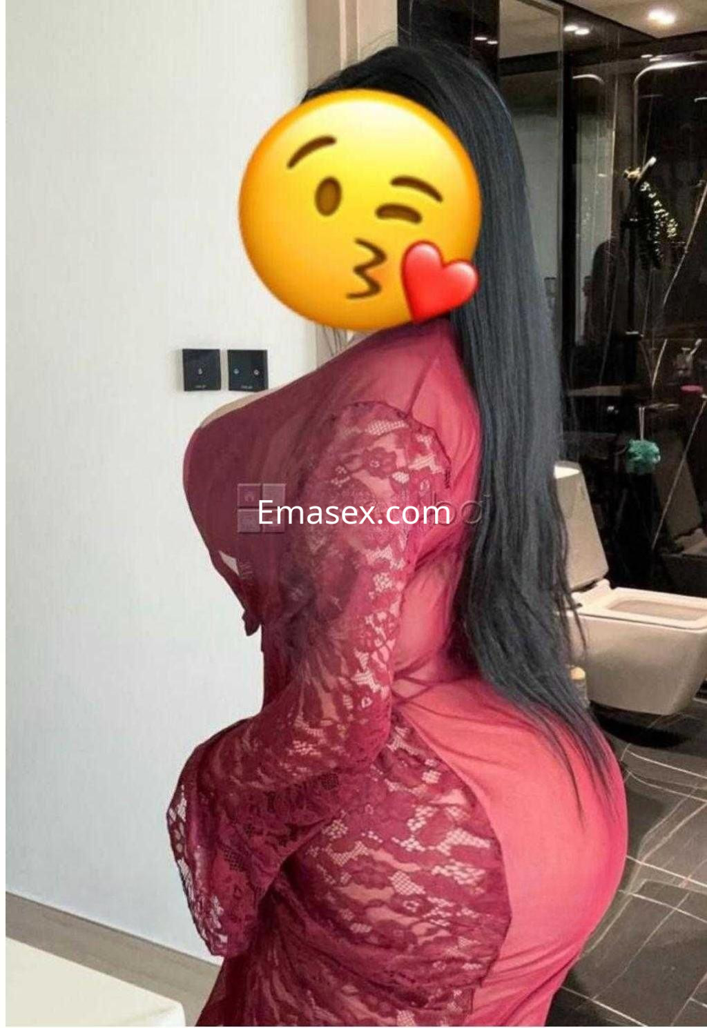 Escort en Madrid luciendo un vestido rojo con encaje, posando de perfil en un ambiente moderno y elegante.