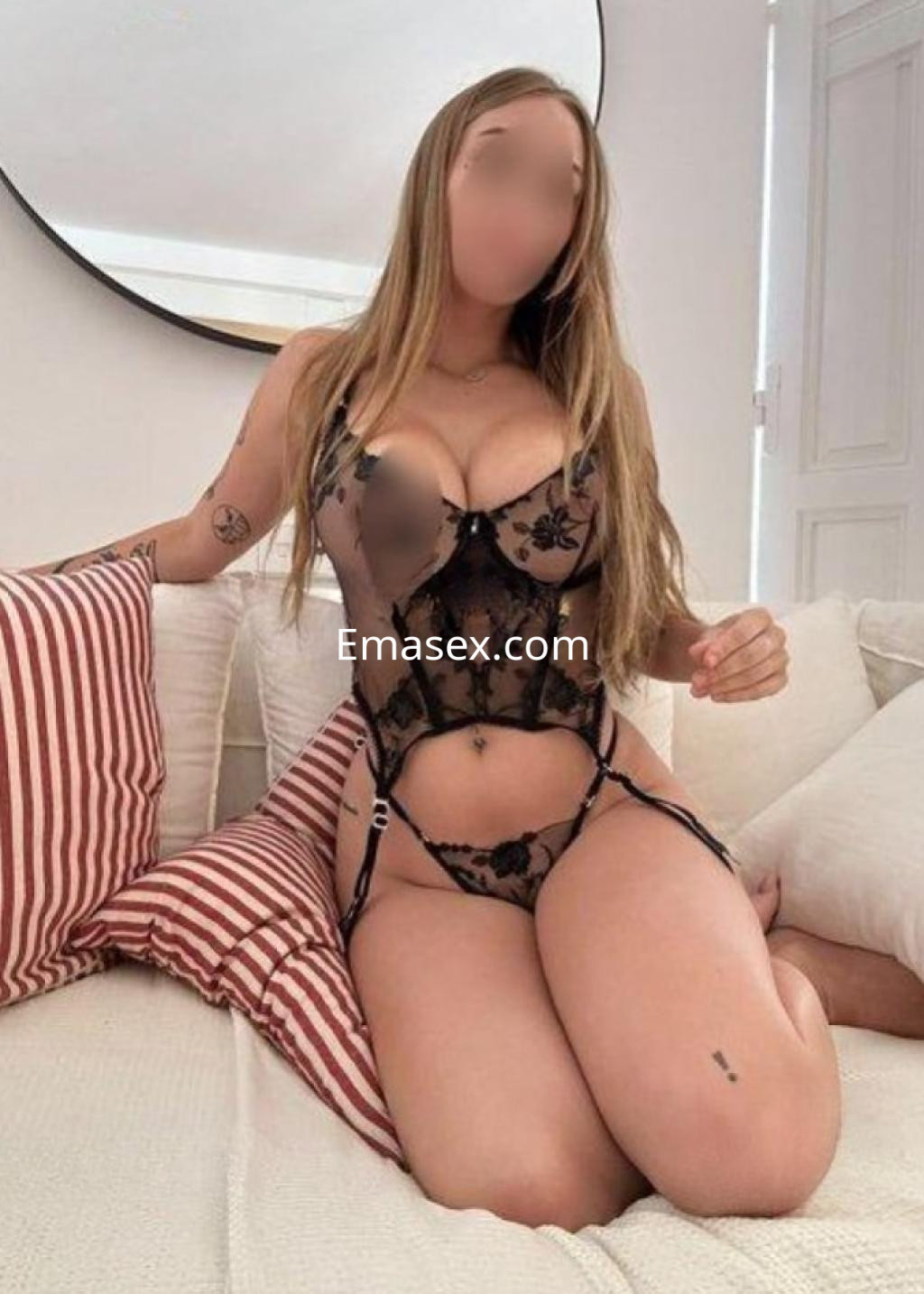 La escort viste un conjunto de lencería negra con detalles florales, posando en un sofá en Burgos.