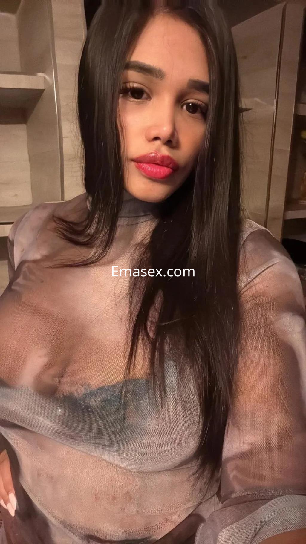 Escort en Alicante con cabello largo y oscuro, vistiendo una blusa transparente que revela lencería negra.