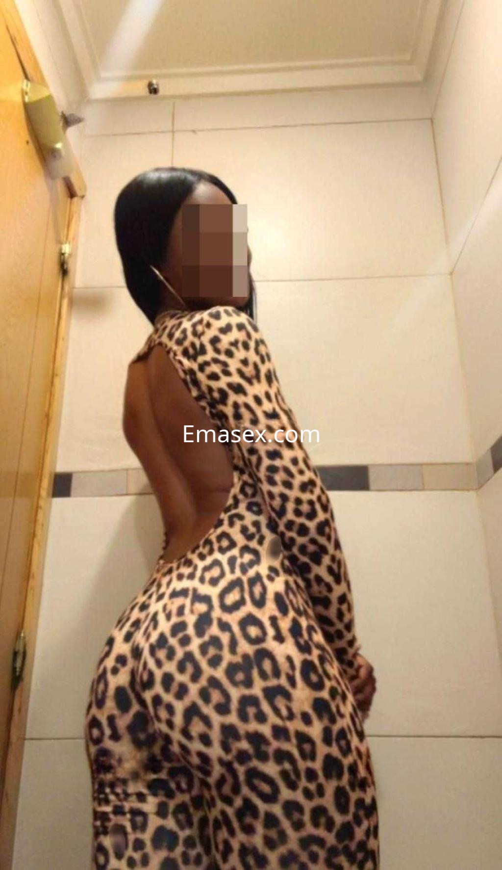 Escort de piel oscura con cabello lacio, luciendo un ajustado mono de leopardo en un entorno interior de León.