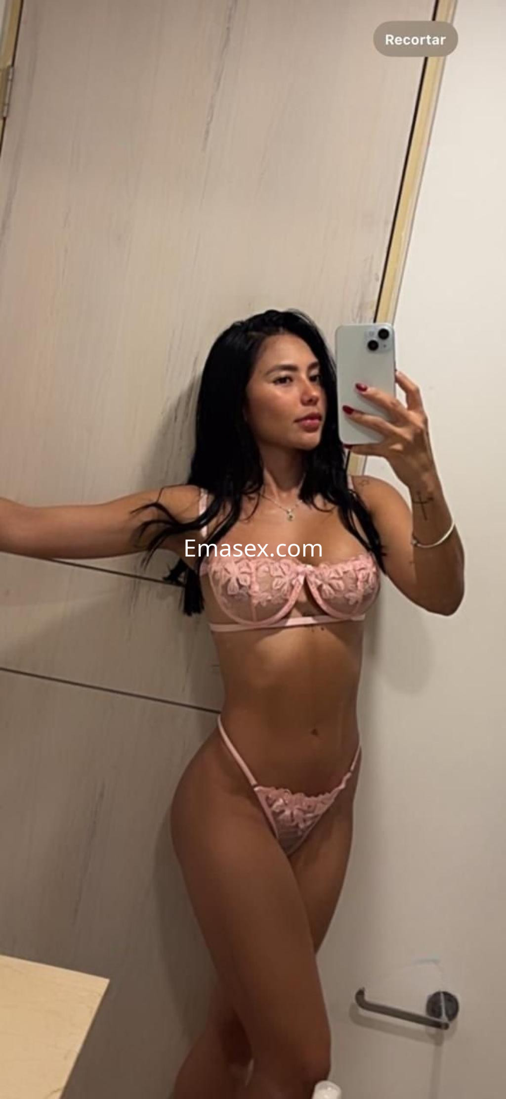 Escort de Zaragoza posando frente al espejo con lencería rosa y cabello largo y oscuro.