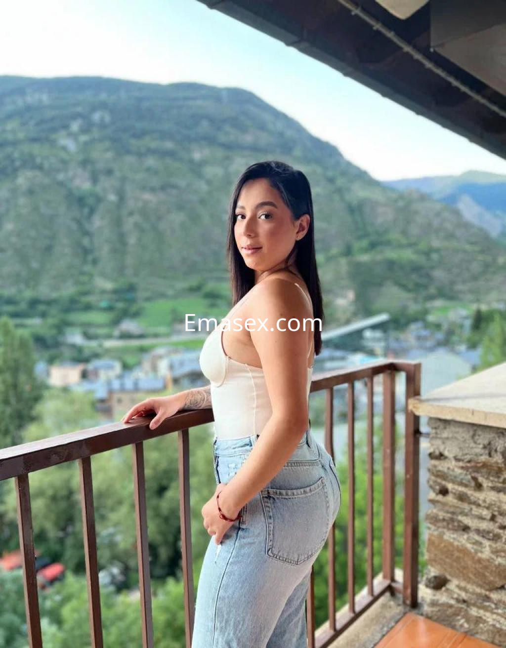 Puta posando en un balcón con vista a la montaña, lleva una blusa blanca y jeans ajustados en Lleida.