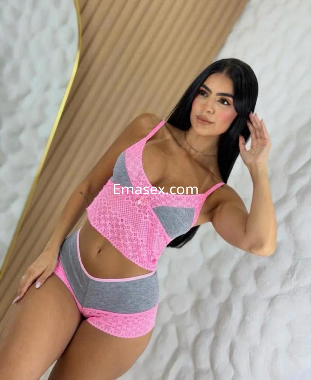 Escort en Granada posando con un conjunto de lencería gris y rosa, con cabello largo y lacio, en un fondo neutro.