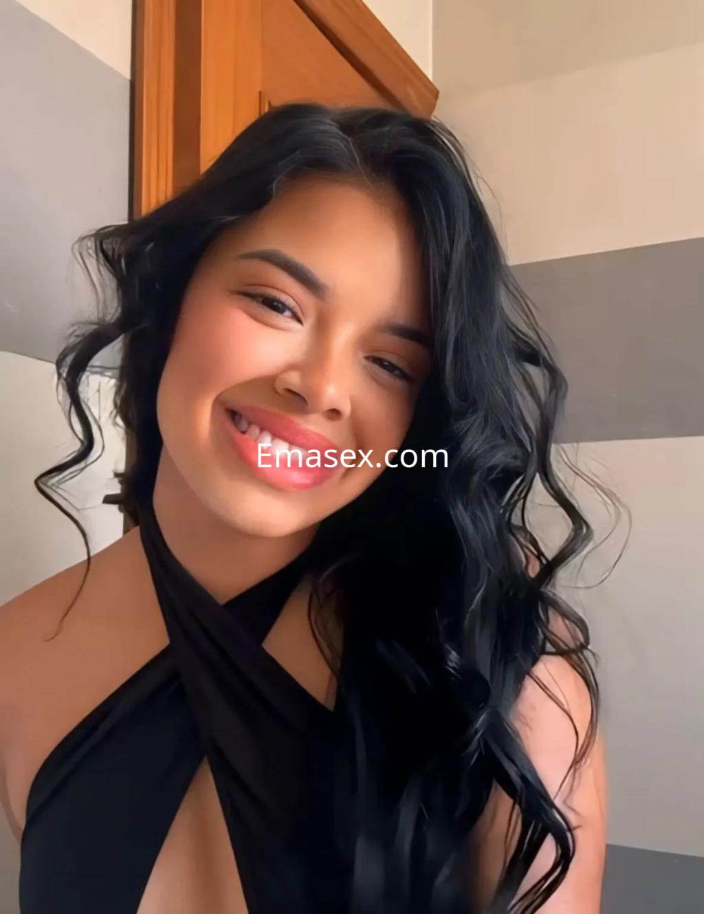Escort en Palma de Mallorca, con cabello largo y ondulado, sonríe vestida con un top negro ajustado.