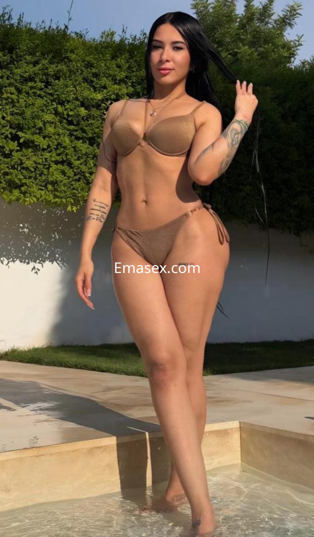 Escort en Madrid posa en una piscina, luciendo un bikini marrón y mostrando su piel bronceada y tatuajes.