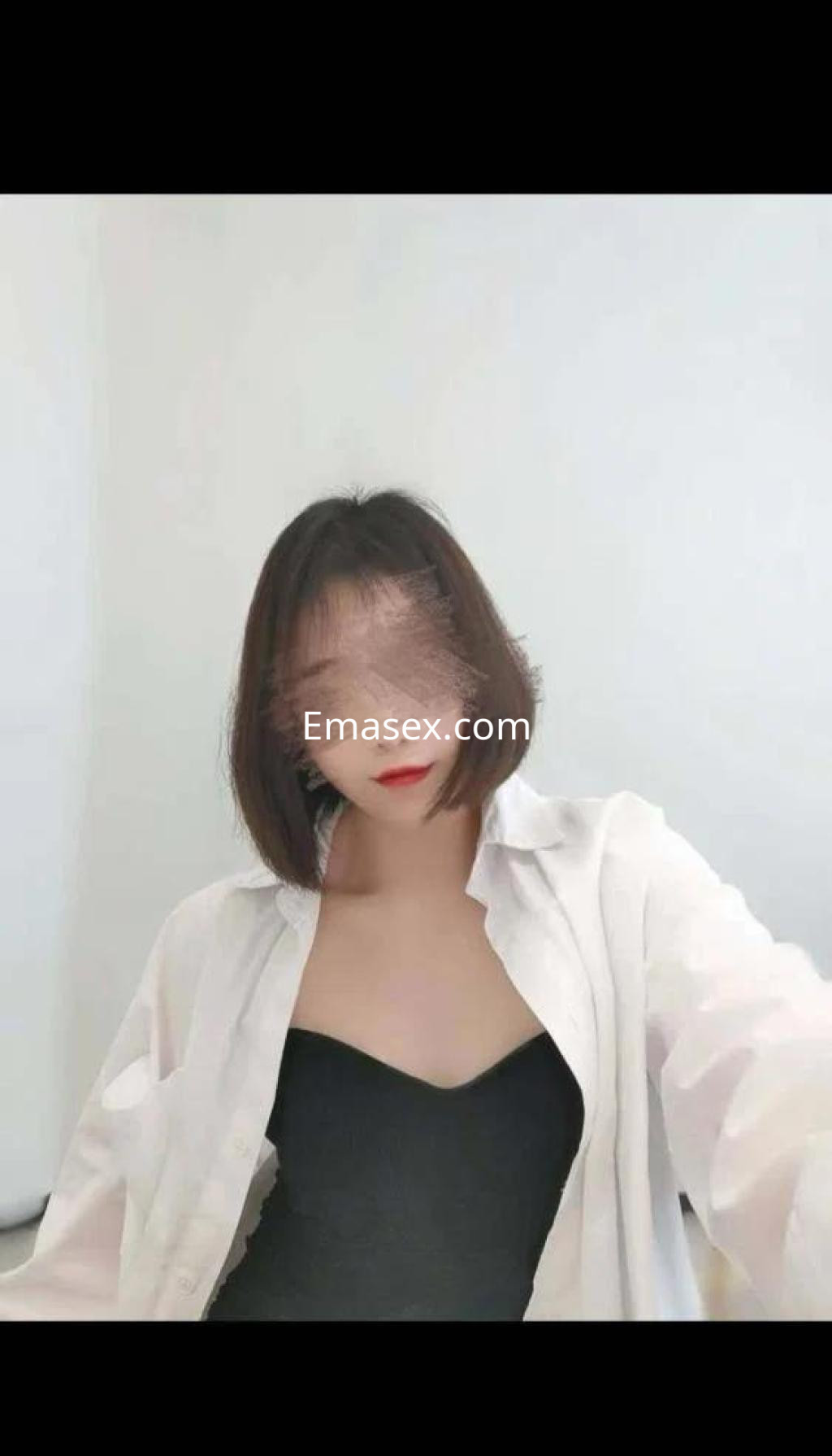 La puta en Madrid lleva una blusa blanca abierta sobre un body negro, con cabello corto y un fondo claro.