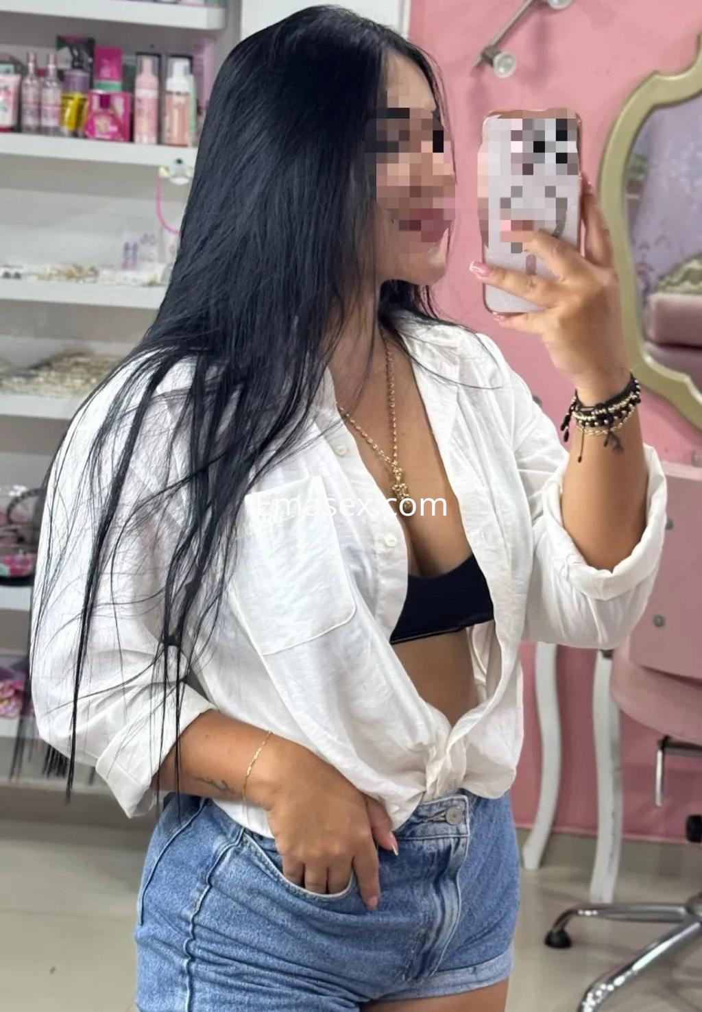 Escort en Albacete con cabello largo y lacio, viste una blusa blanca abierta y shorts de mezclilla.