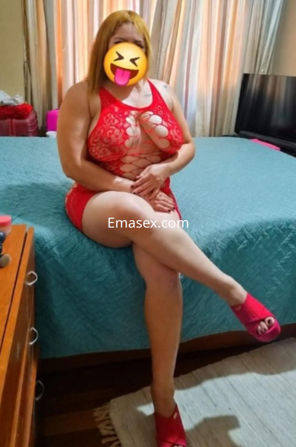 Puta con cabello rubio, usando un conjunto rojo de encaje y sandalias, sentada en la cama en Coruña.