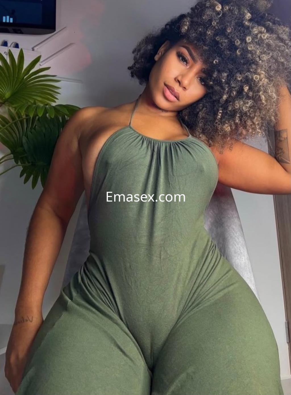 Escort en Coruña con cabello rizado y suelto, vistiendo un mono verde ajustado en una pose relajada.