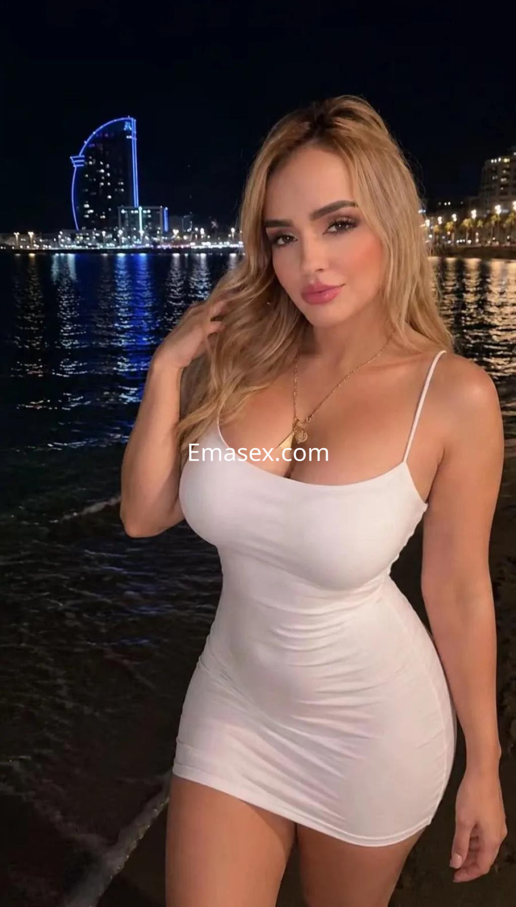 Puta con vestido blanco ajustado, cabello rubio suelto, posando junto al agua en una noche iluminada en Murcia.