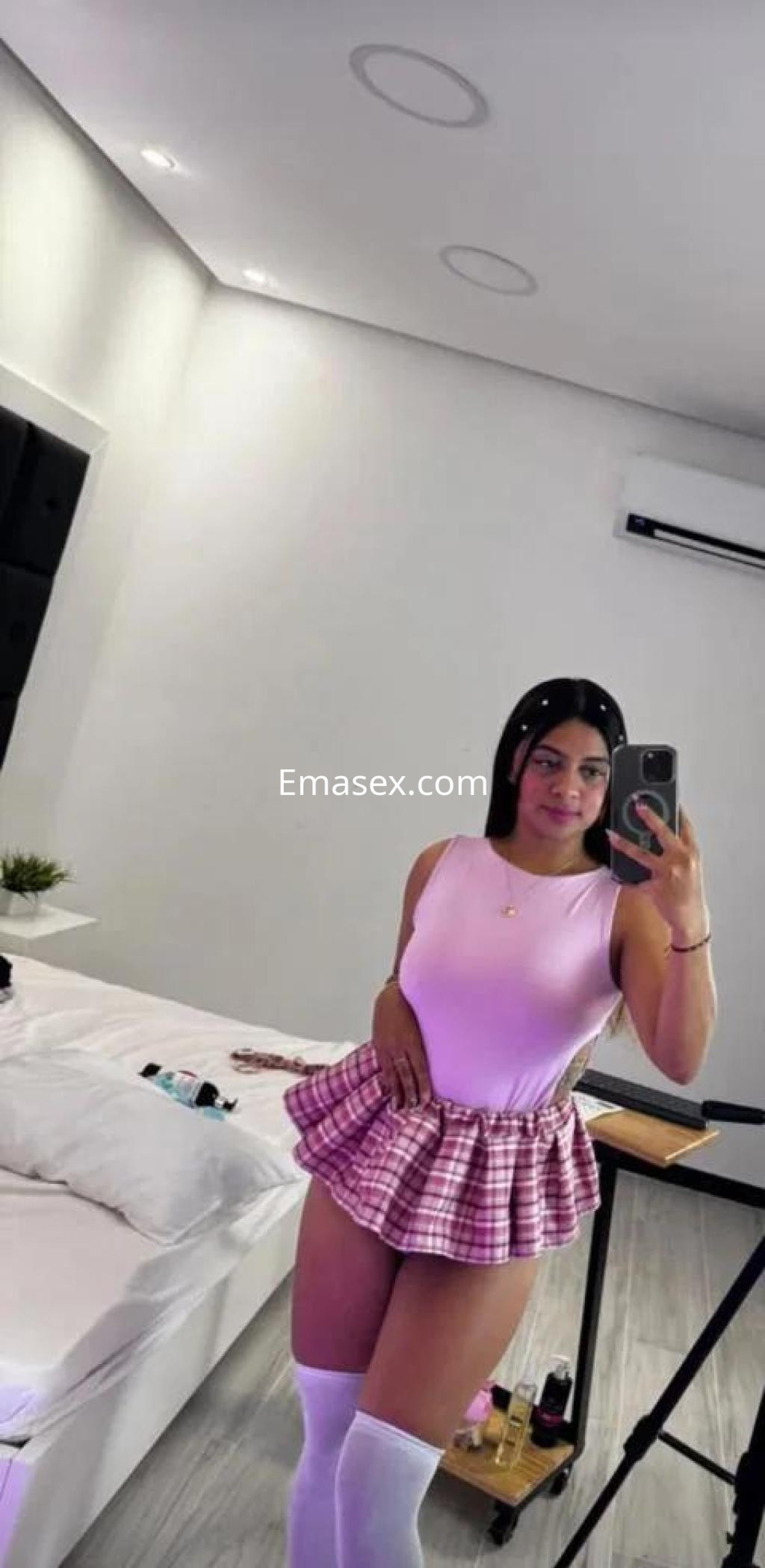 La puta posa en un cuarto con un body rosa y una falda de cuadros, mostrando sus medias blancas en Ourense.