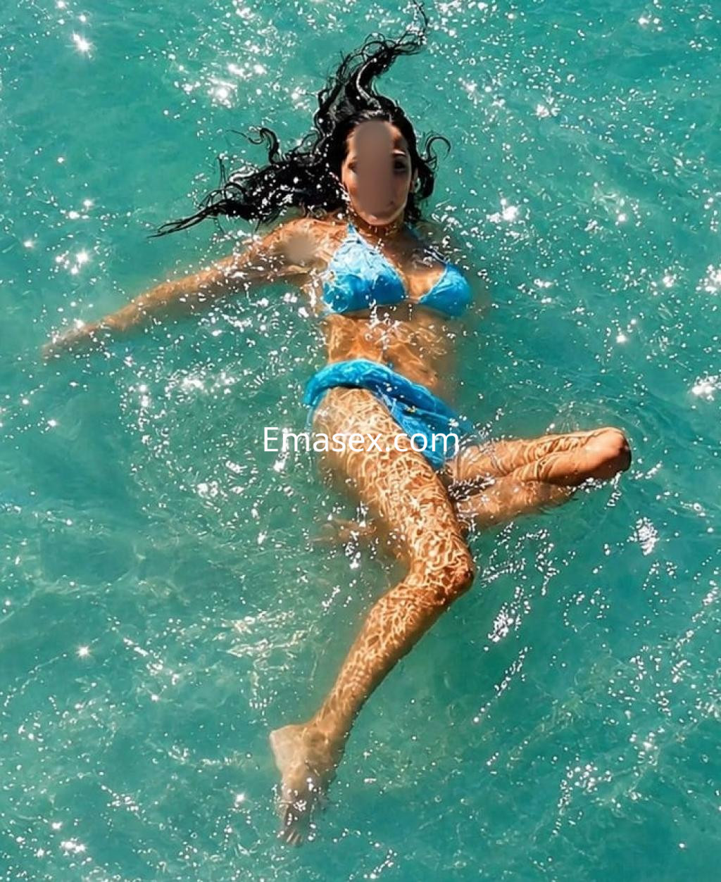 Escort en Irún con bikini azul, flotando en el agua cristalina, luciendo cabello largo y ondulado.