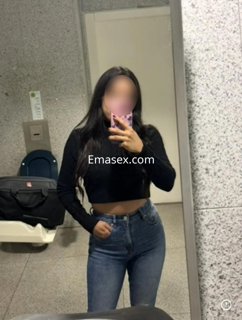 Escort en Santander con cabello largo y oscuro, viste un top negro y jeans ajustados, posando en un espejo.
