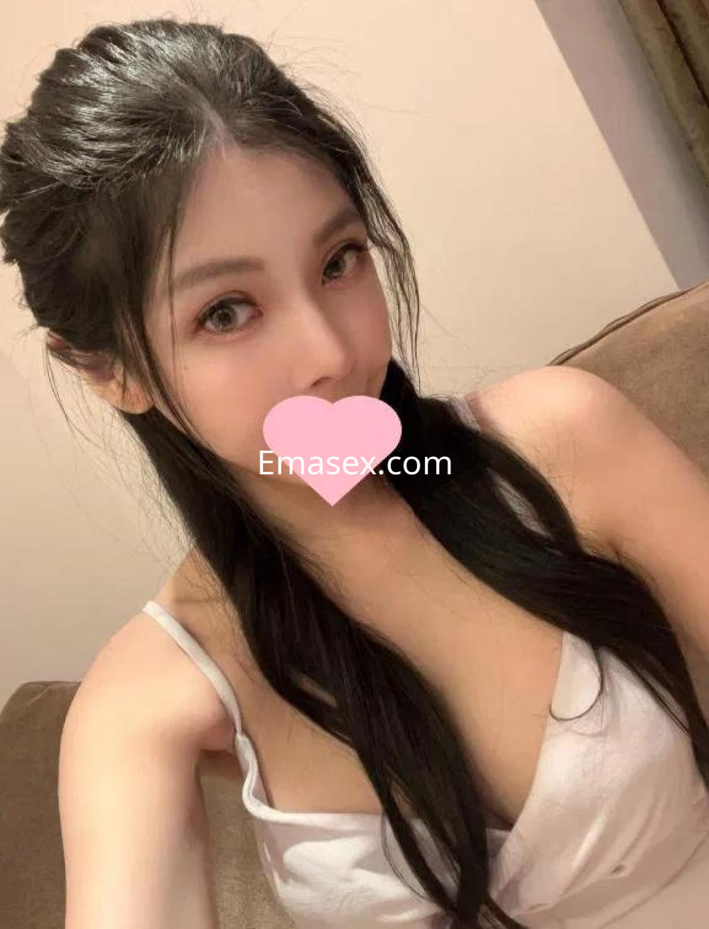 Escort en Barcelona con cabello negro, lacio y largo, vistiendo una blusa blanca, posando en un sofá.
