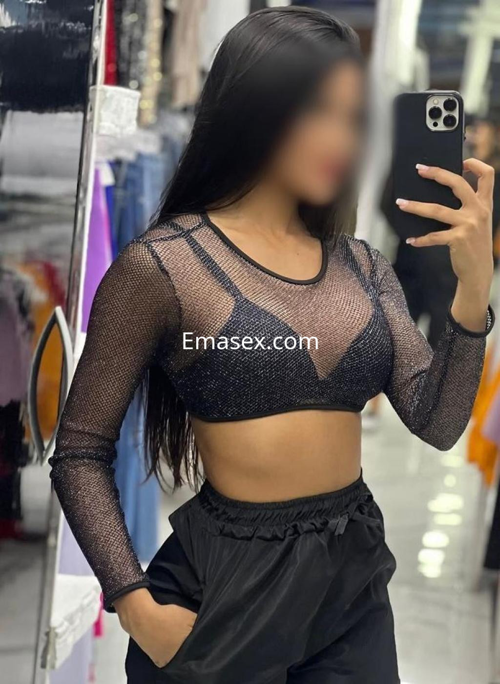 Puta en Badajoz con blusa de malla negra y pantalones oscuros, posando frente a un espejo.