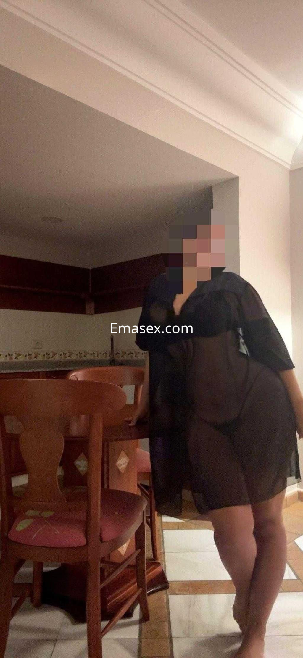 Escort en Tenerife, luciendo un vestido negro semitransparente y posando en un ambiente interior.