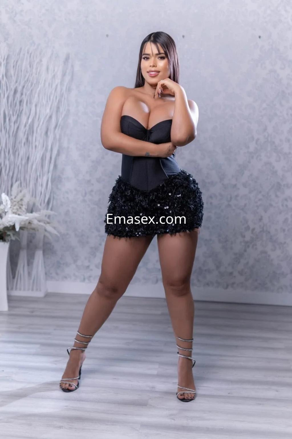 Puta posando en Alicante con un corset negro y una falda corta brillante, mostrando confianza y sensualidad.