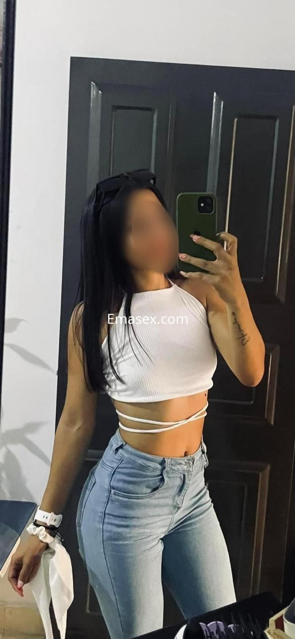 La puta posa frente al espejo en un top blanco ajustado y jeans de tiro alto, mostrando su figura en Ibiza.