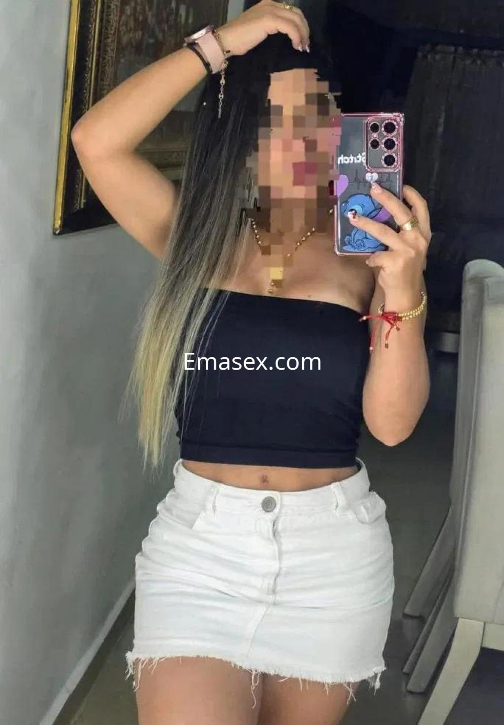 Puta en Madrid con top negro ajustado y falda blanca corta, posando frente a un espejo en un ambiente acogedor.