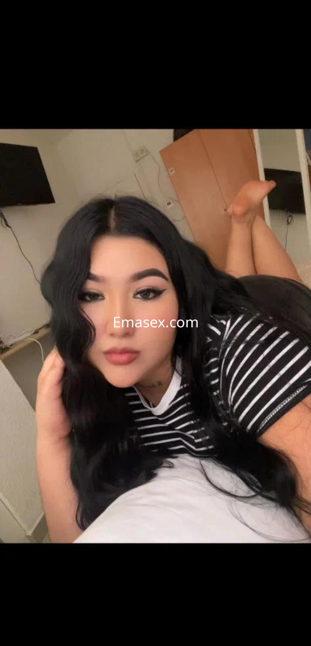 Escort en Córdoba, con cabello largo y ondulado, posando en una cama con una camiseta de rayas.