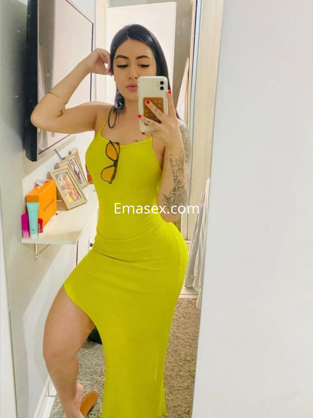 Escort en Zamora, posando frente al espejo con un vestido amarillo ajustado y gafas en la cabeza.