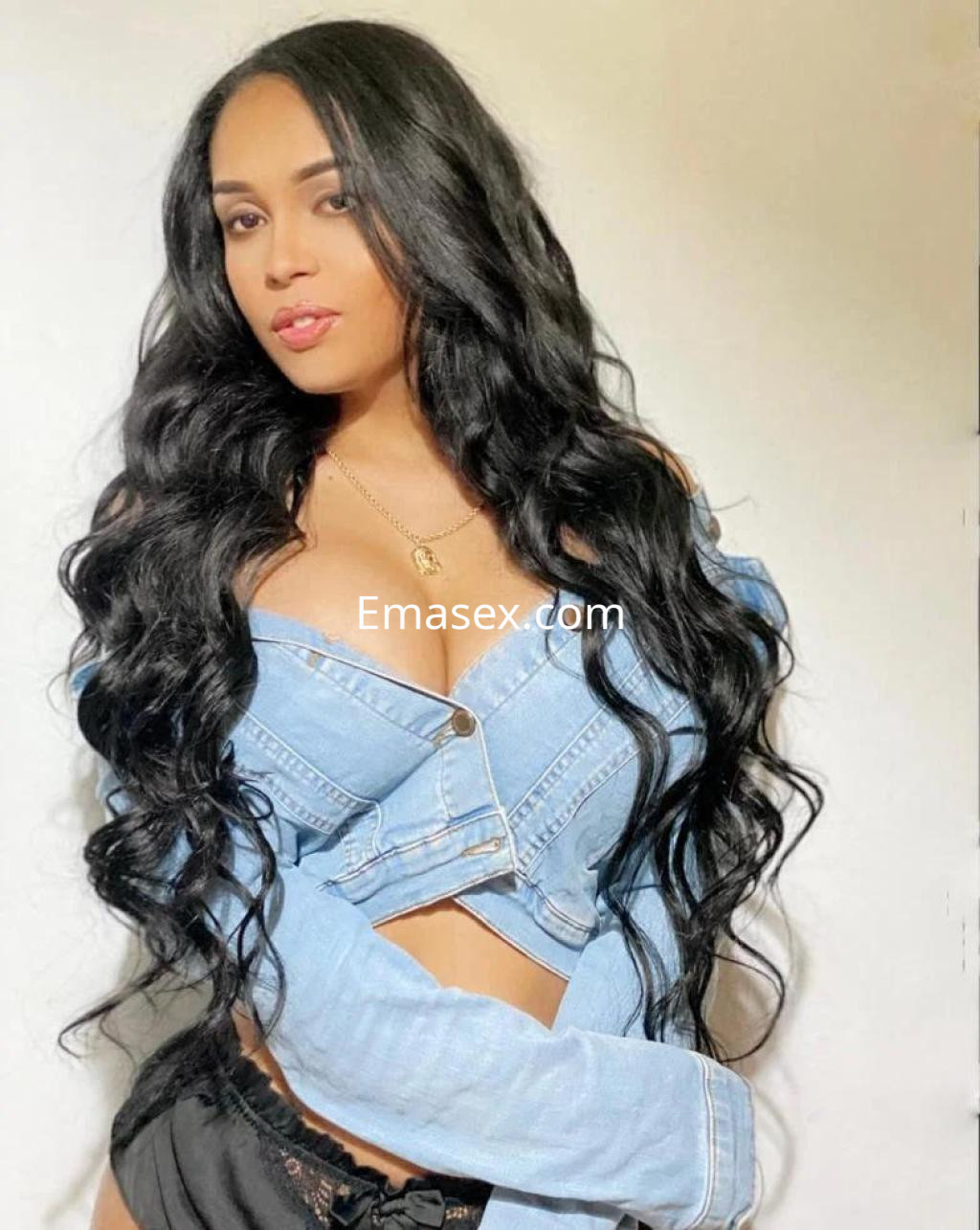Escort en Córdoba con cabello largo y ondulado, vistiendo una chaqueta de jean y pantalones cortos oscuros.