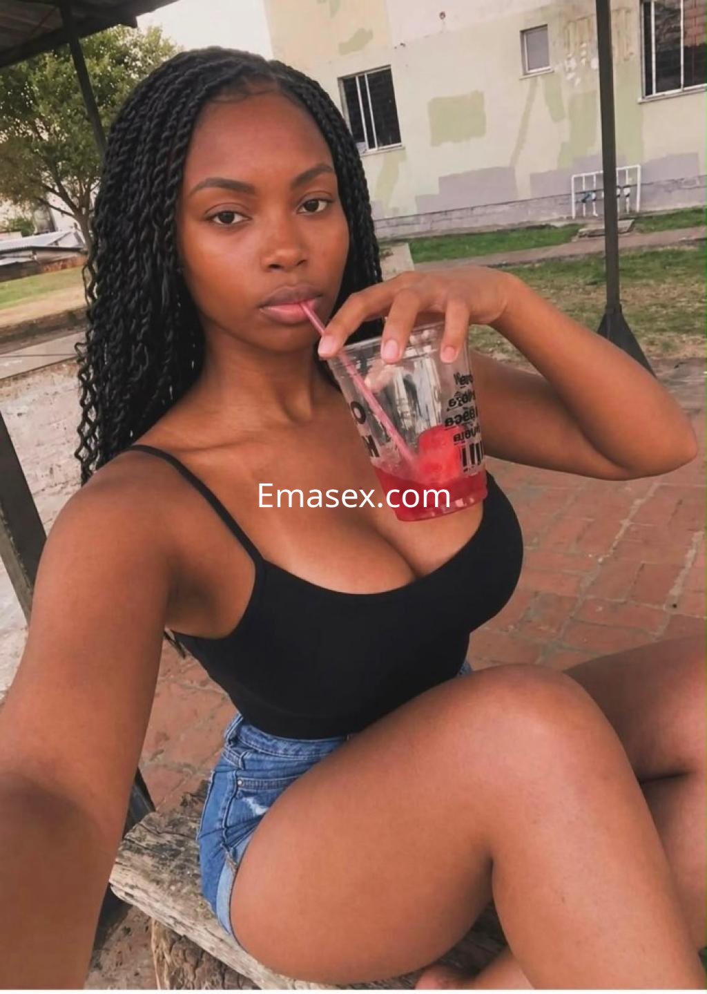 La puta en Coruña viste una camiseta negra y shorts de mezclilla mientras sostiene un vaso con bebida.
