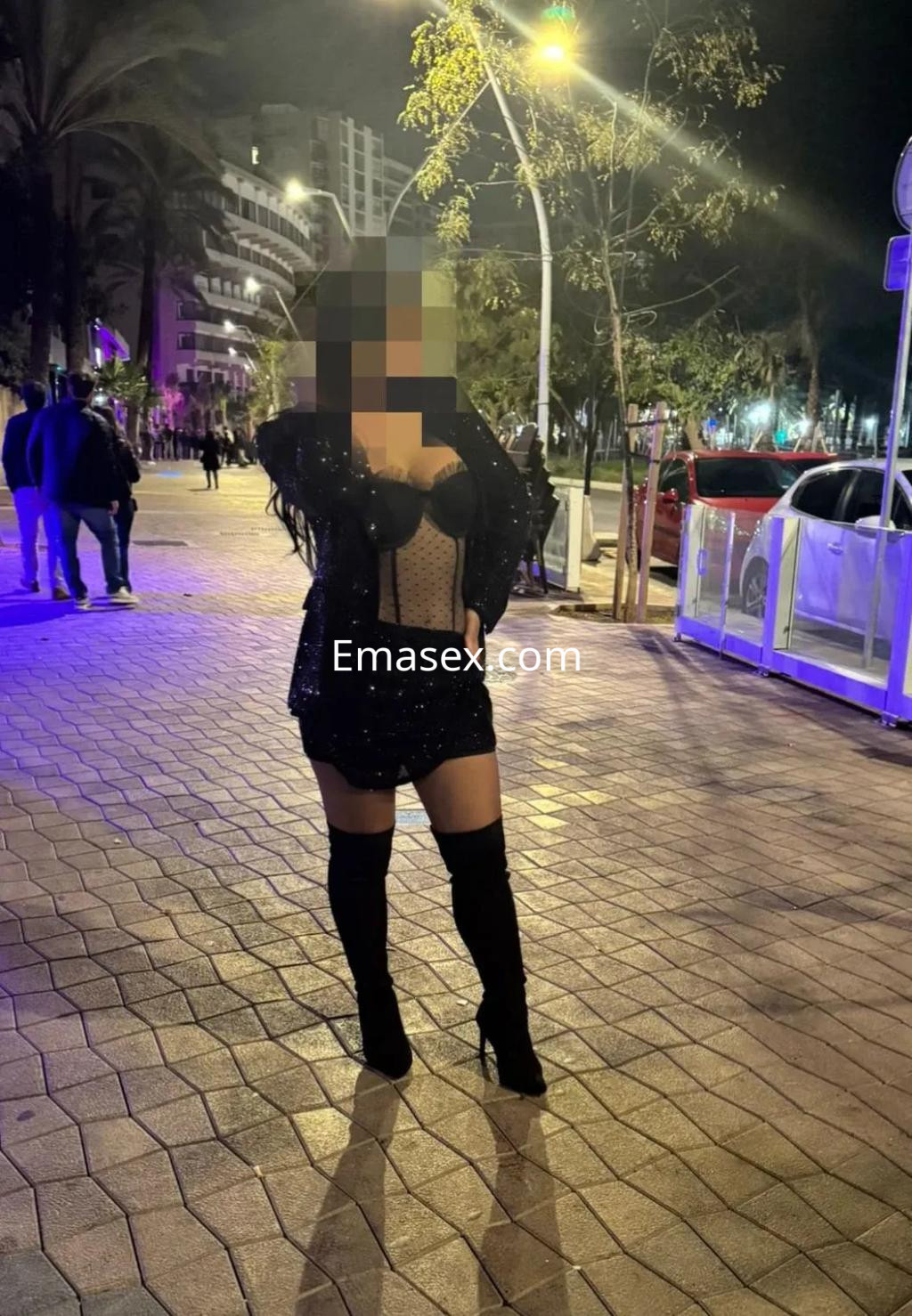 Escort posando en la calle de Zaragoza, vistiendo un vestido corto brillante y botas altas negras.