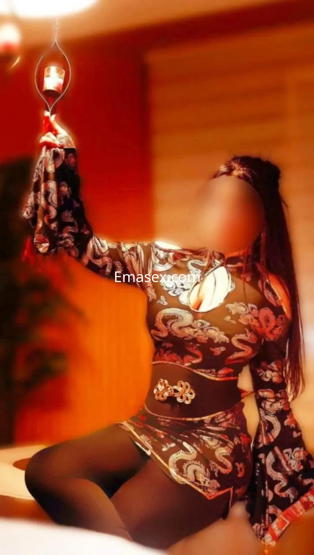 Escort en Zaragoza con un vestido ajustado de manga larga y detalles ornamentales, sentada en un ambiente iluminado.