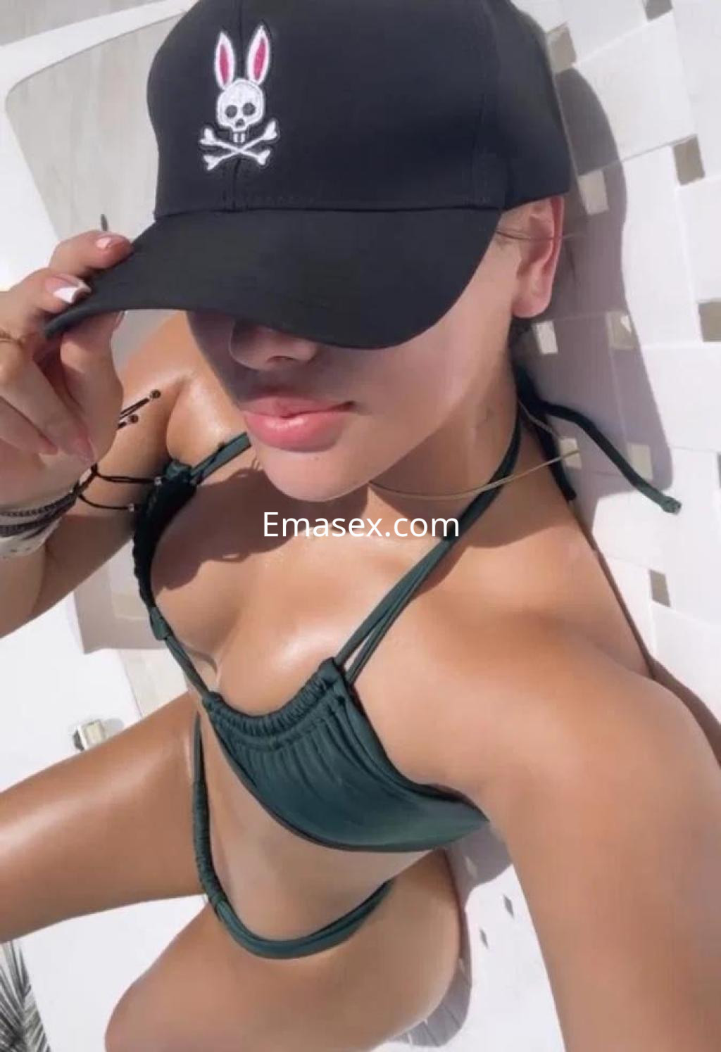 Escort en Las Palmas luciendo un bikini verde y gorra negra mientras toma el sol en una tumbona.