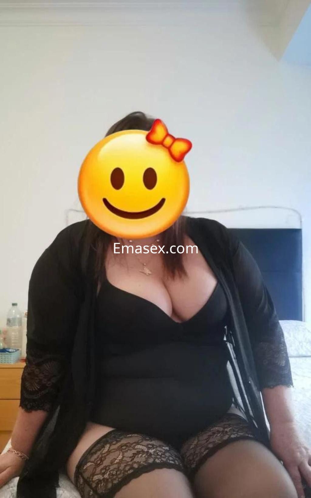 Puta en Córdoba sentada sobre una cama, vistiendo un conjunto negro de lencería con medias y un kimono.