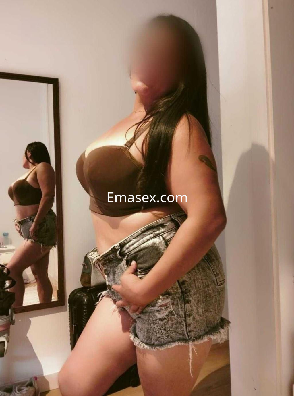 Escort en Alicante posando de perfil con un sujetador marrón y shorts de mezclilla, mostrando su figura.