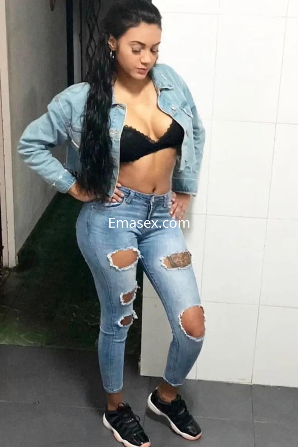 Puta en Vigo luce un conjunto de jeans rasgados y sujetador negro, con chaqueta de mezclilla y zapatillas deportivas.