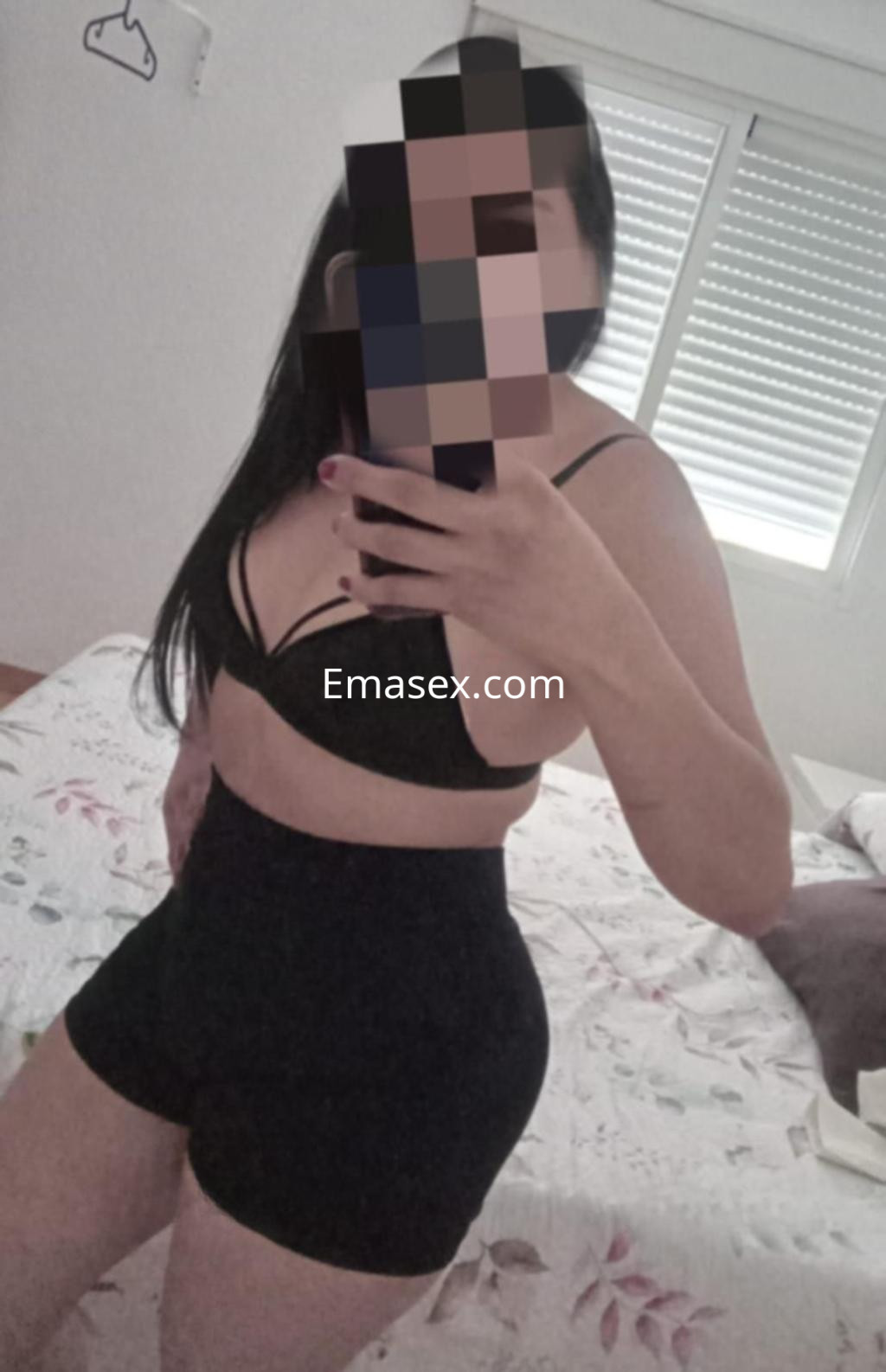 Escort en Madrid mostrando un conjunto de sujetador negro y pantalones cortos, en un ambiente doméstico.