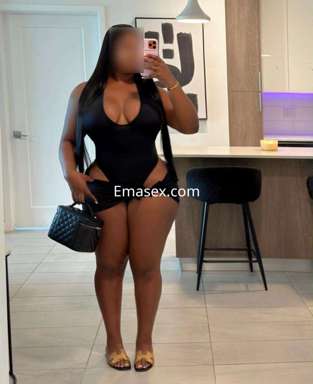 Puta en Granada con un traje de baño negro, posando en un ambiente moderno con un bolso negro.