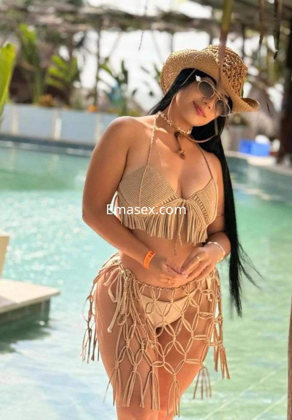Escort en Barcelona luciendo un bikini de crochet beige y un sombrero de paja junto a una piscina.