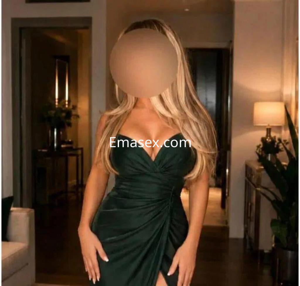 Escort en León luciendo un vestido verde ajustado, con escote pronunciado y cabello largo y rubio.