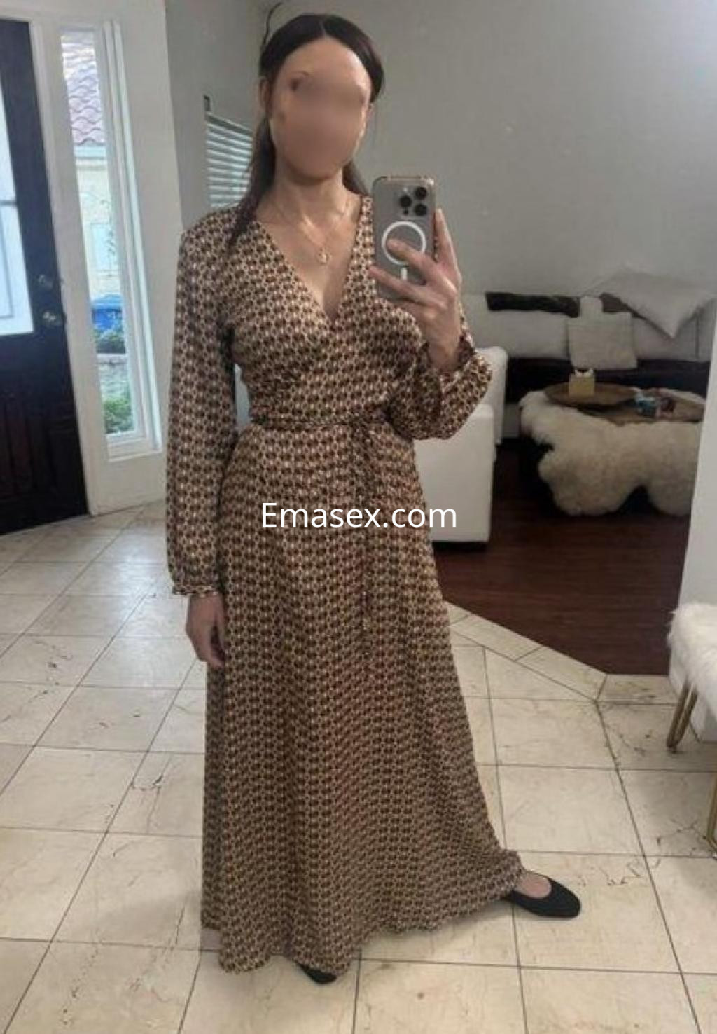 Escort en Madrid con vestido largo de estampado floral, posa frente a un espejo en un espacio luminoso.