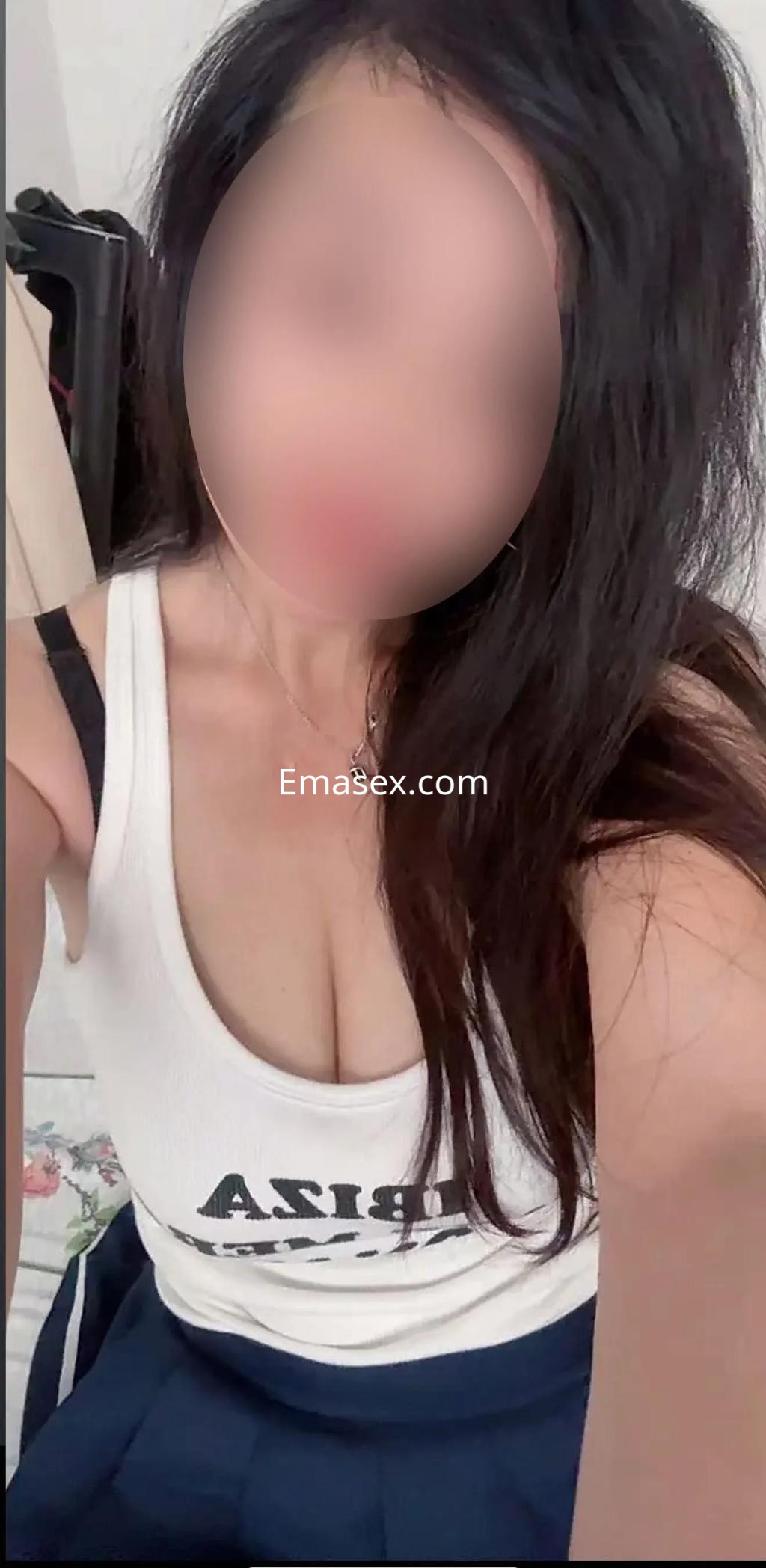Escort en Zaragoza con cabello largo y oscuro, viste una blusa blanca y una falda corta, posando de forma atractiva.