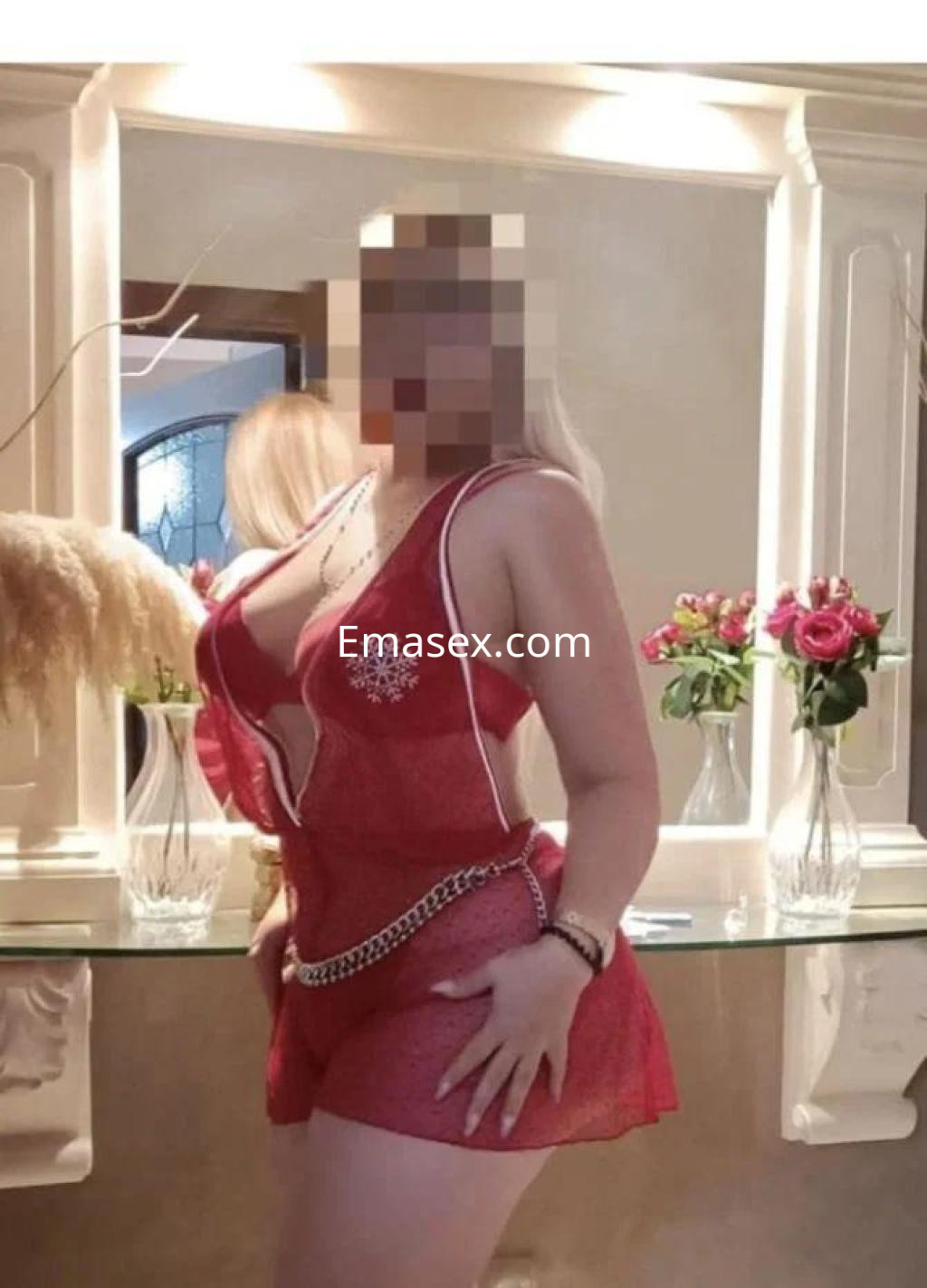 Escort en Zamora luciendo un vestido rojo transparente con detalles brillantes, posando frente a un espejo.