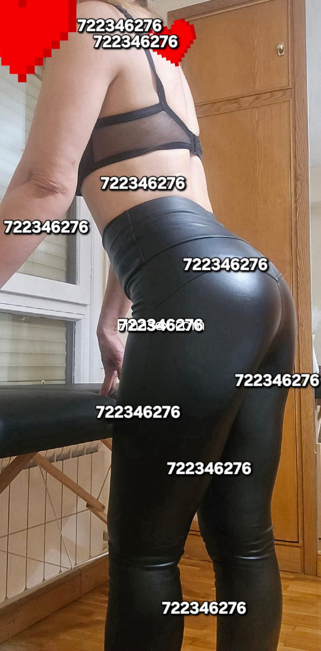 Escort en Pamplona vistiendo un sujetador de encaje y leggings de cuero, posando de perfil en un interior.