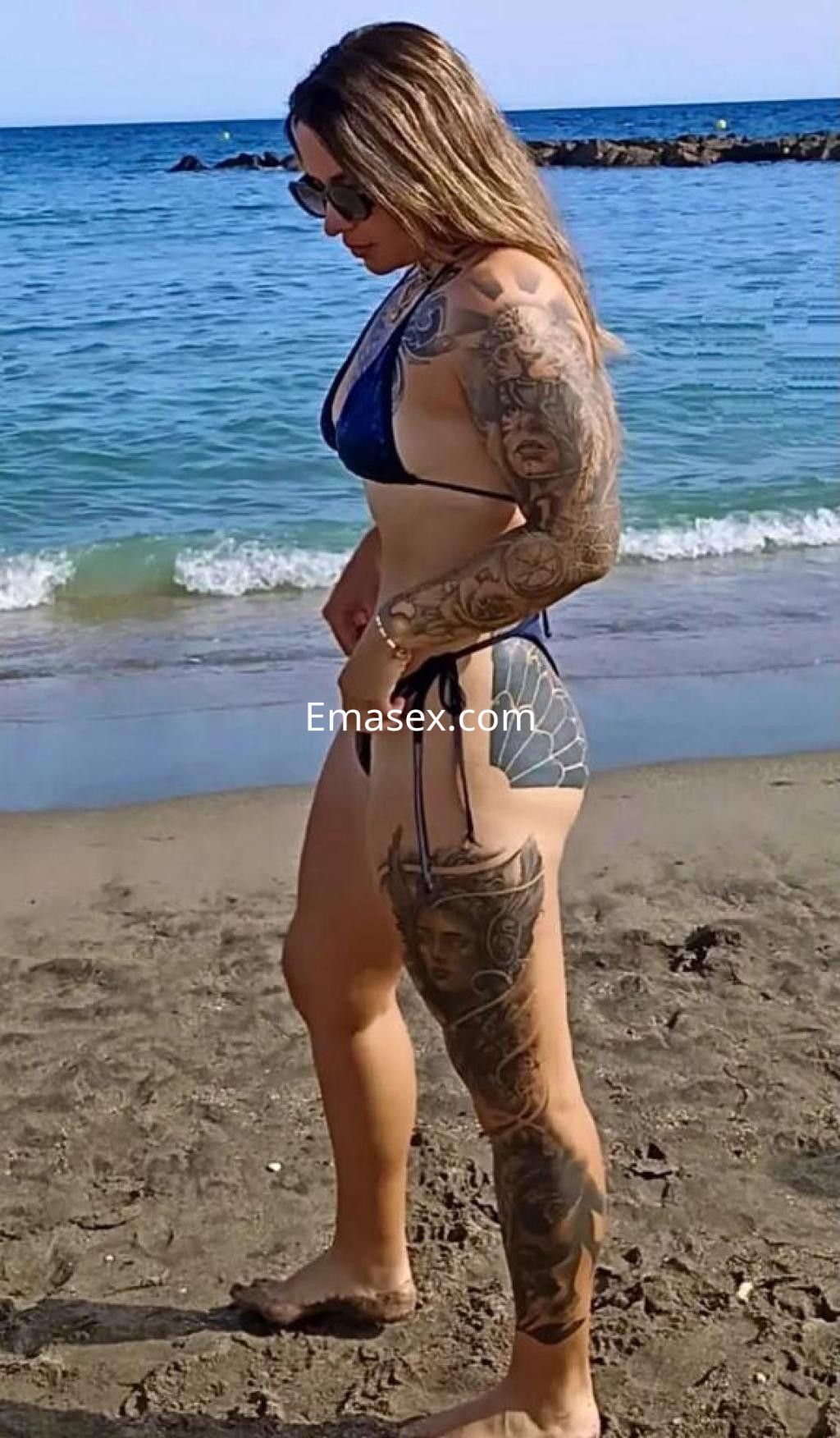 La escort en Las Palmas luce un bikini azul y exhibe sus tatuajes mientras camina por la playa.
