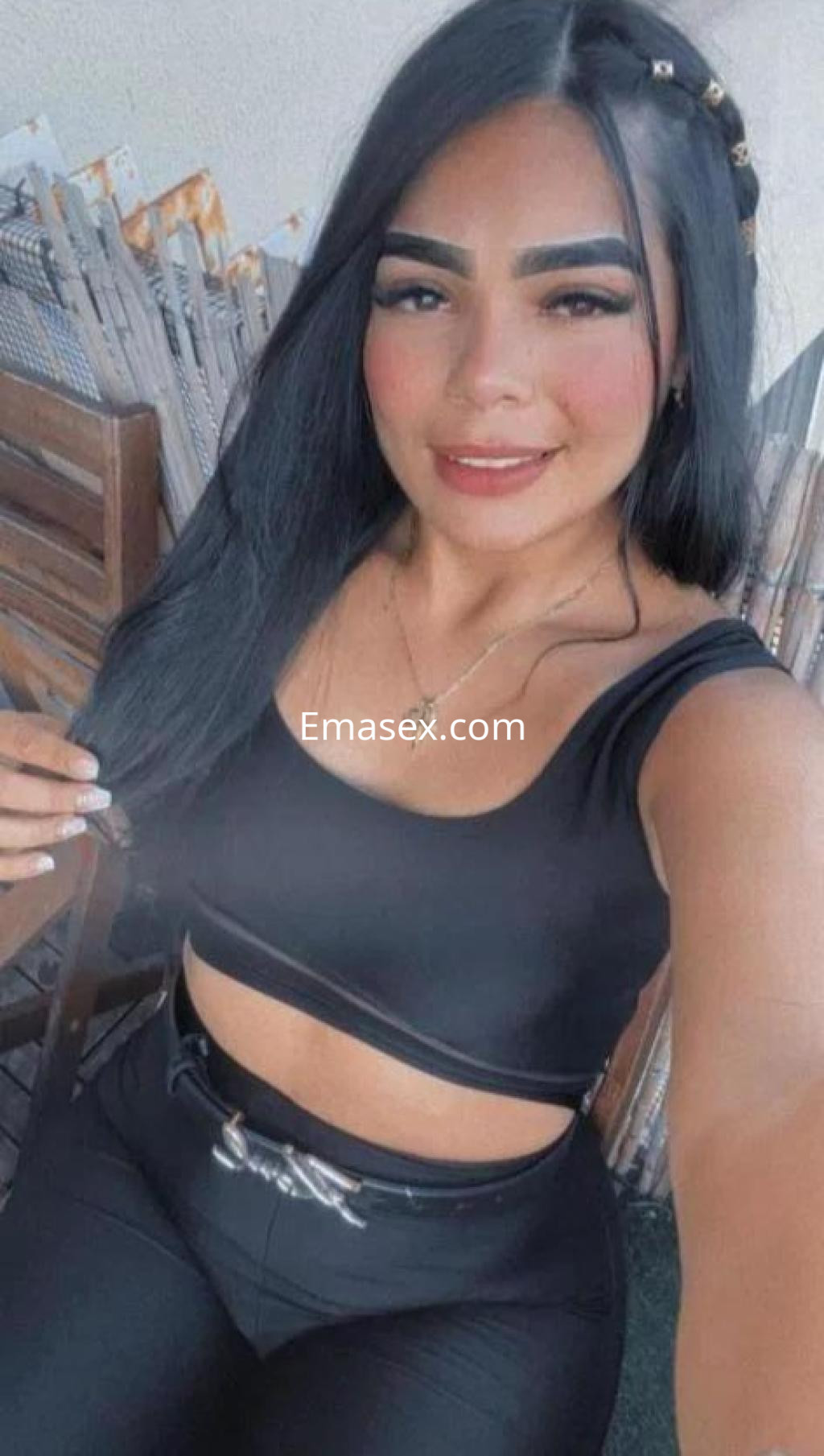Puta con cabello largo y lacio, vistiendo un top negro y pantalones ajustados, sonríe en un ambiente informal en Valencia.