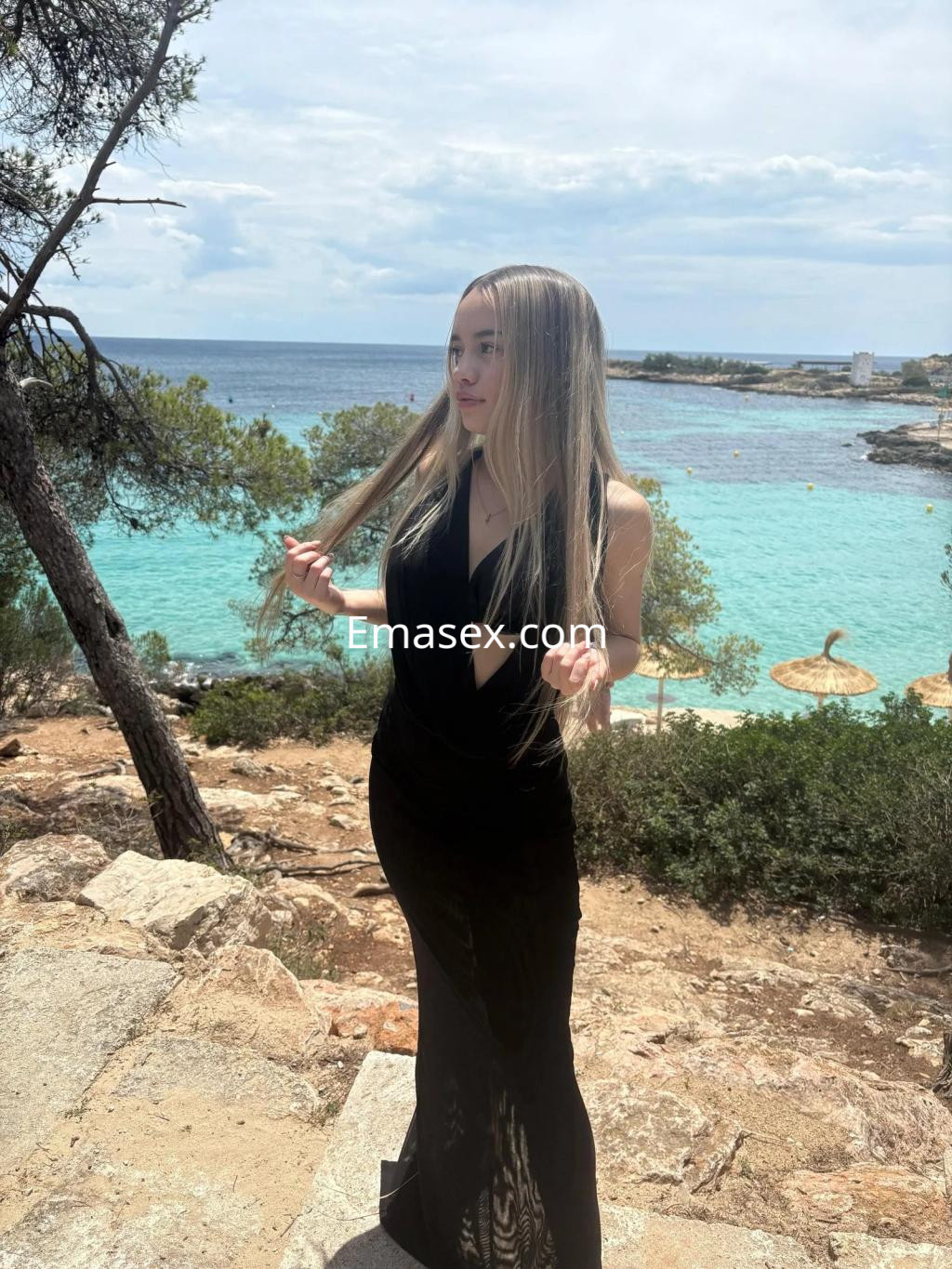 Escort de cabello lacio y rubio, vestida con un vestido negro, posando junto al mar en Palma de Mallorca.