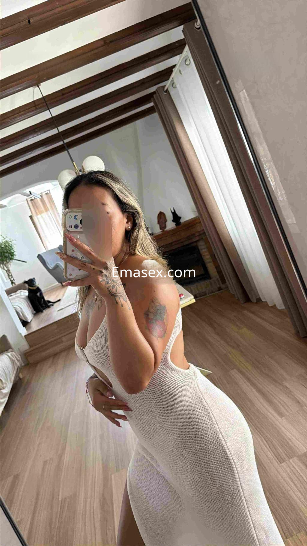 Puta posando en un vestido blanco ajustado, con cabello largo y ondulado, en un ambiente luminoso de Málaga.