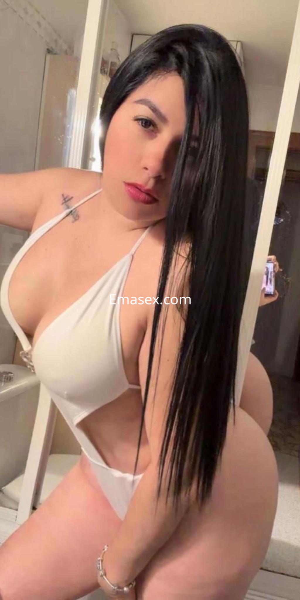 Puta con cabello largo y negro, vistiendo un bañador blanco que resalta su figura, posando en un baño en Murcia.