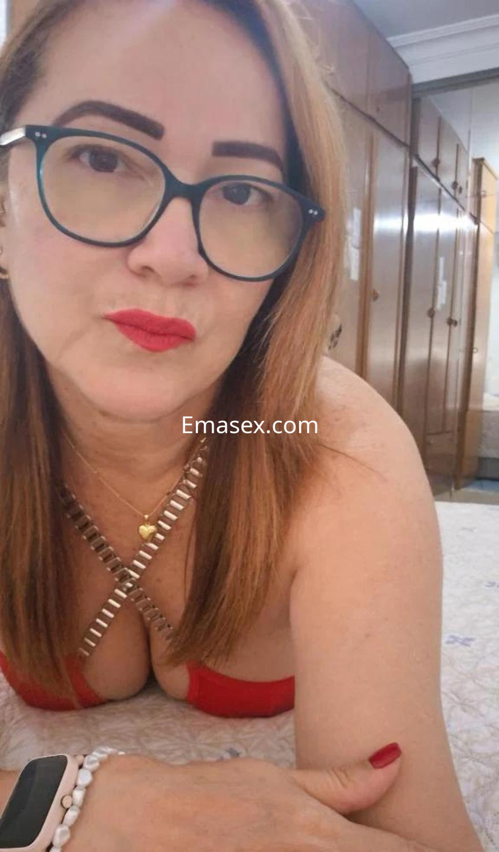 Puta en Huelva con cabello largo y lacio, usando un top rojo y accesorios, posando en un ambiente interior.