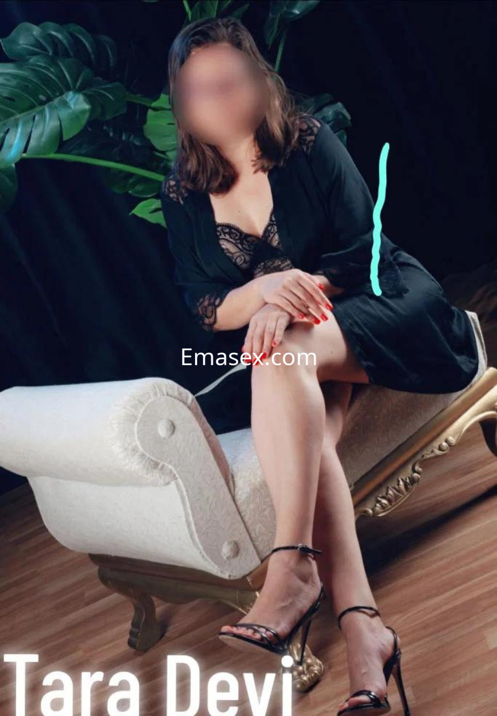 Escort en Las Palmas sentada en un sofá elegante, vistiendo una bata negra y lencería con detalles en encaje.