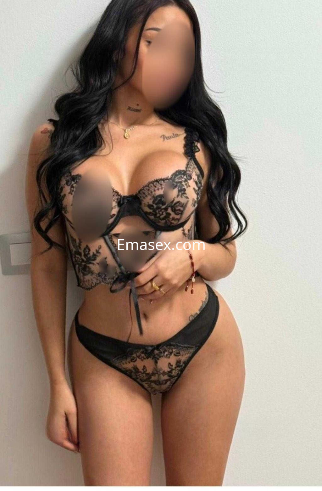 Puta en Cádiz, luciendo un conjunto de lencería negra con detalles de encaje, posando de pie y sonriendo.