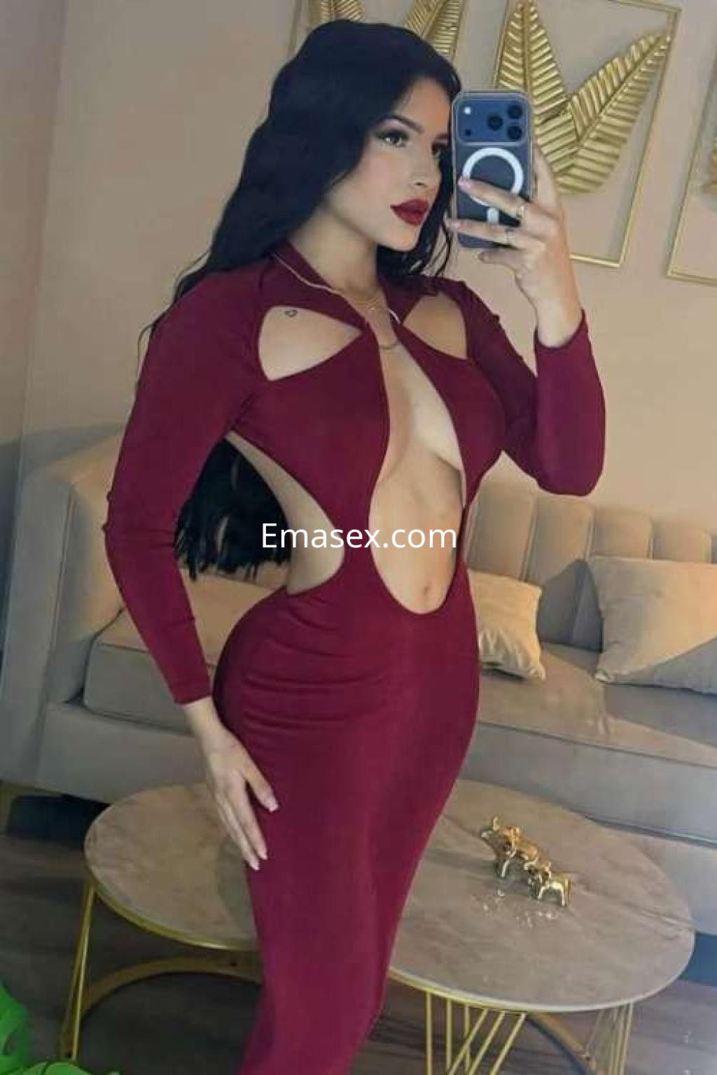 Escort en Ibiza con vestido largo rojo de diseño atrevido, posando frente a un espejo en un ambiente moderno.